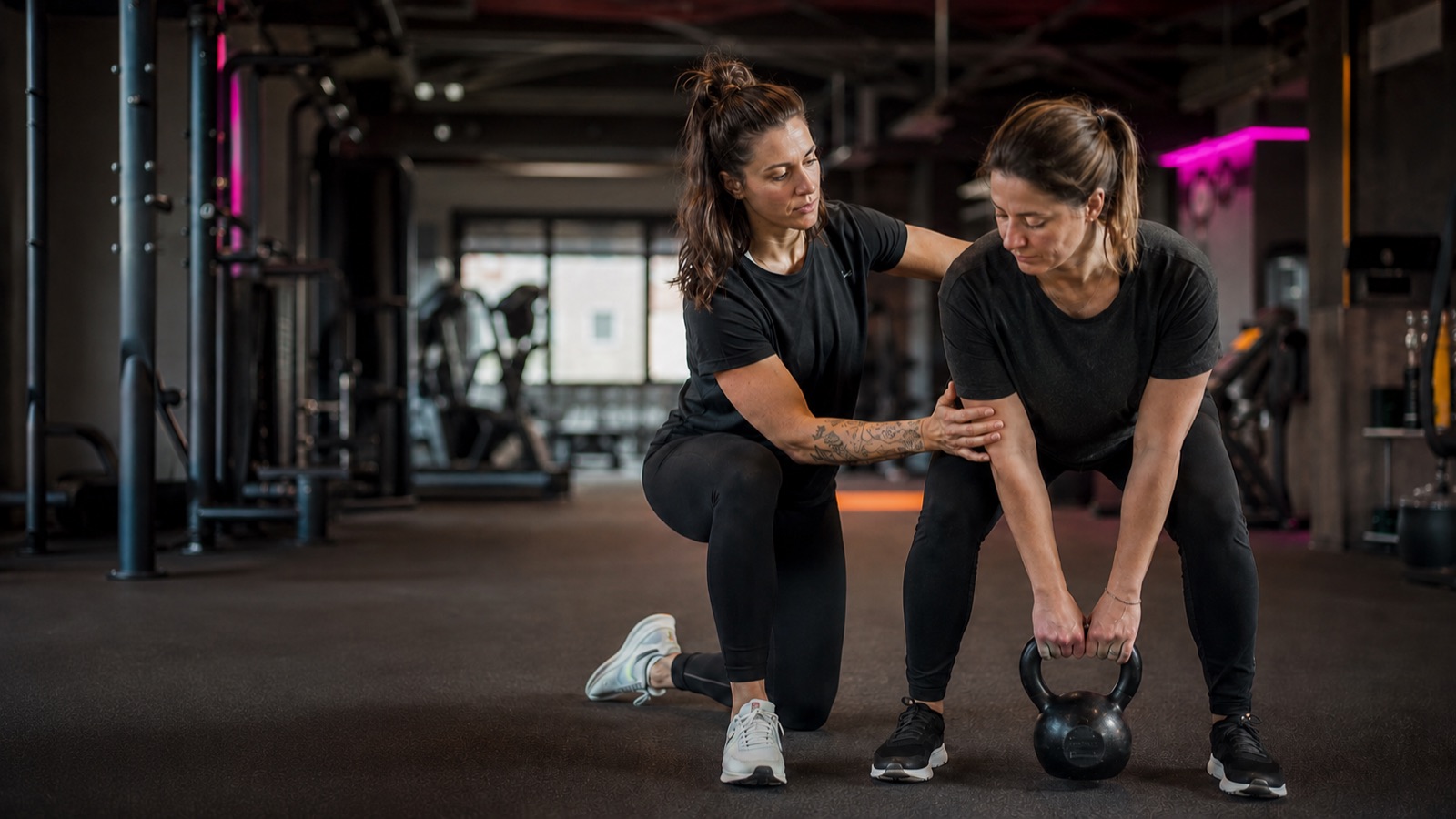 Coach corrigeant la posture d'une cliente pendant un soulevé de kettlebell